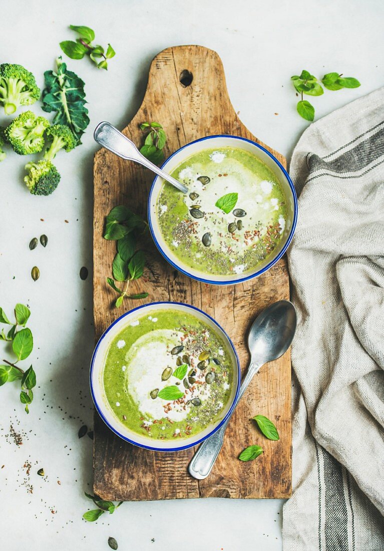 Spring detox broccoli green cream soup with mint and coconut cream in blue bowls on rustic wooden board
