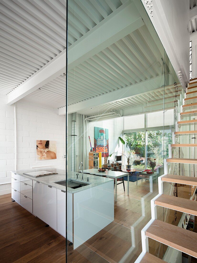 Glaswand zwischen offenem Wohnraum mit Kücheninsel und Treppenhaus mit freitragender Treppe