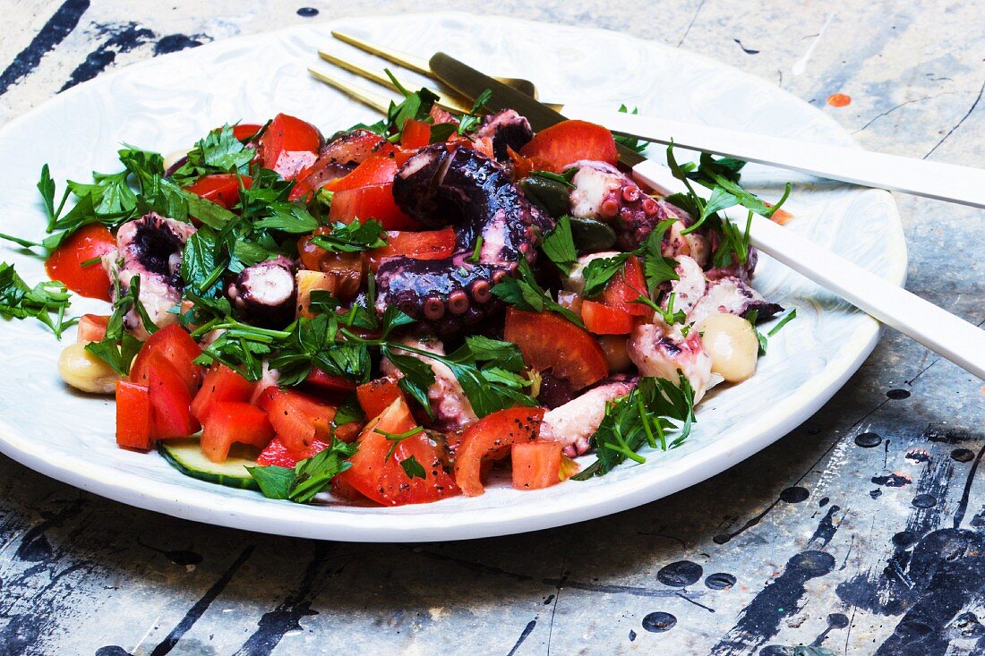 Octopus salad with tomatoes, parsley and white beans on a plate with cutlery