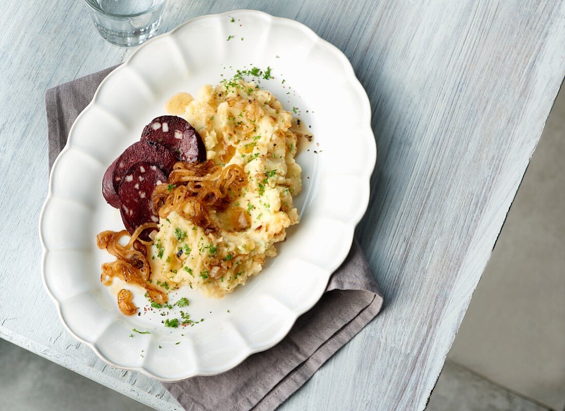 Onion and potato mash with fried blood sausage slices and roasted onions