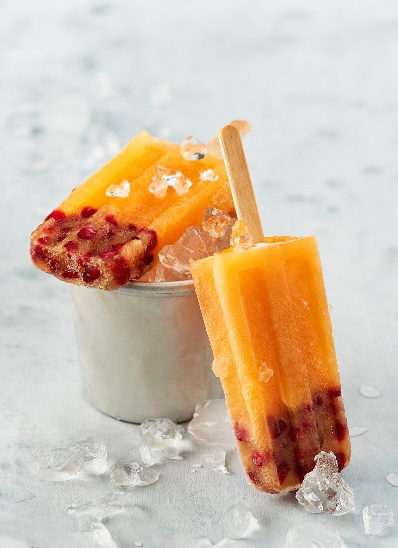 Mango and pomegranate ice lollies on sticks with crushed ice