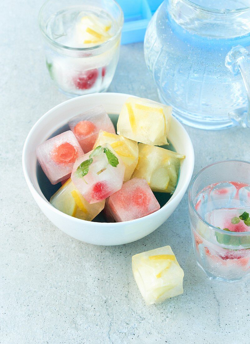 Sommerliche Fruchteiswürfel in Wasserschale und in Gläsern