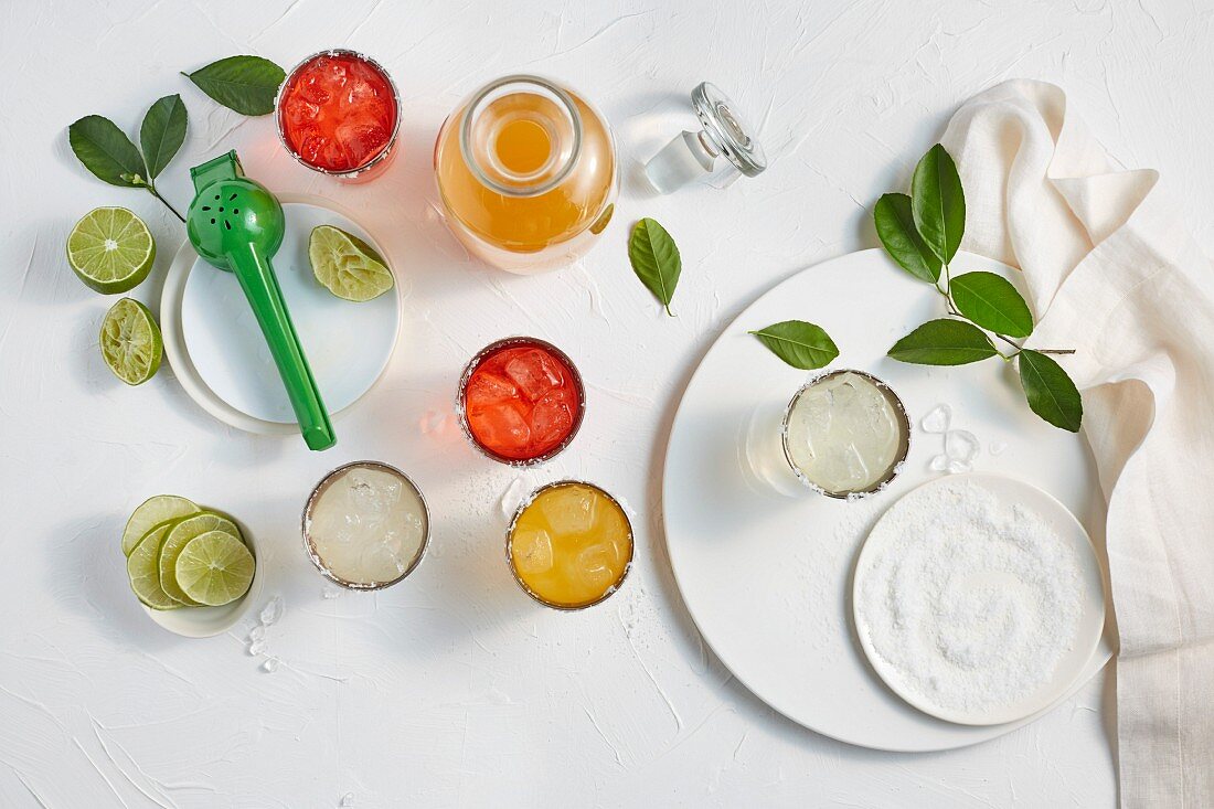 Assorted flavors of Margaritas in glasses on a white surface with salt and limes