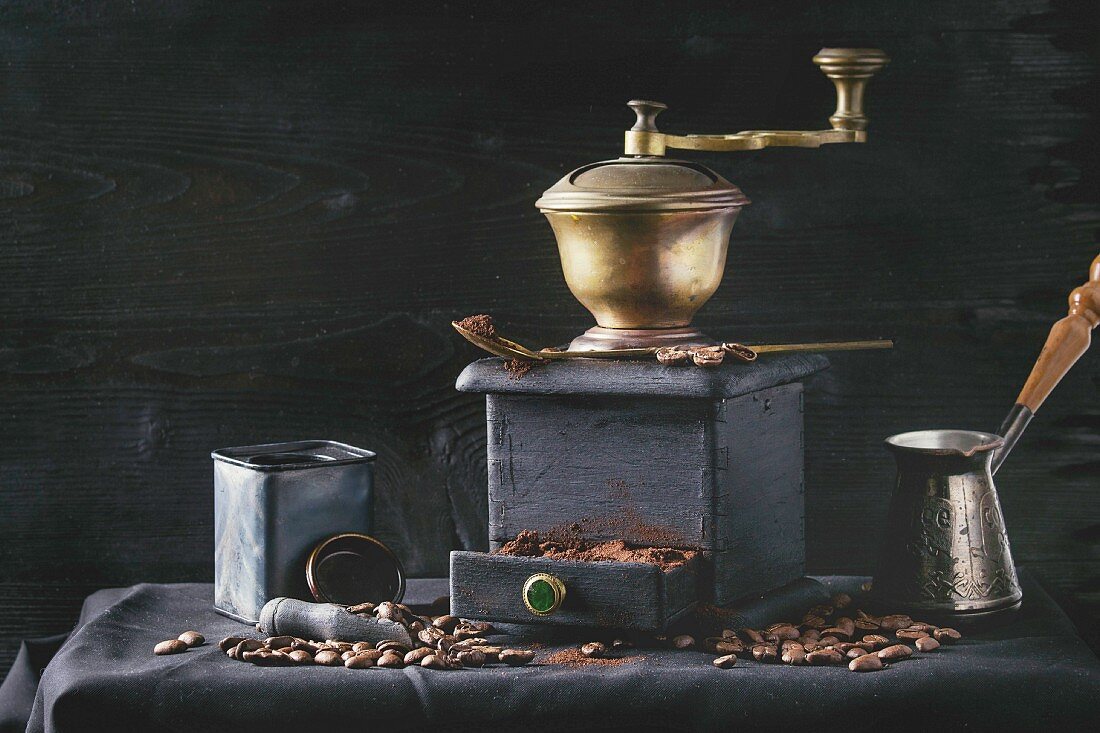 Old vintage grinder with roasted coffee beans and grind coffee in tin jar with scoop over black table with black wooden background