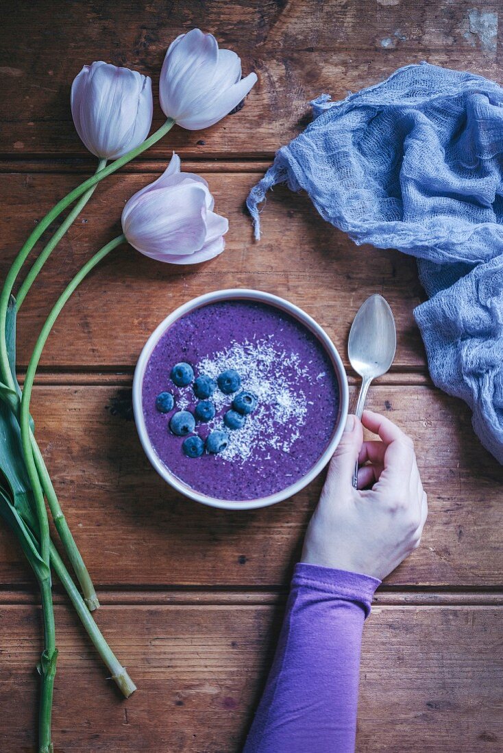 Woman eating a blueberry smoothie bowl on a rustic wooden table