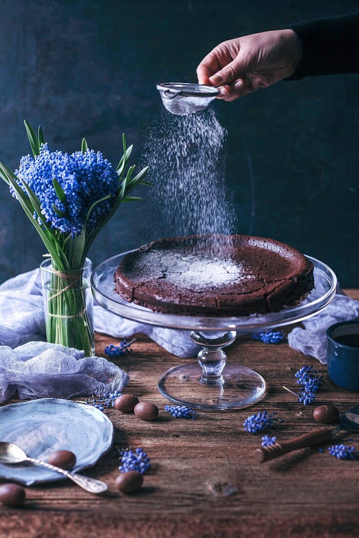 Woman sprinkling powdered sugar on top of Swedish chocolate cake on a cake stand