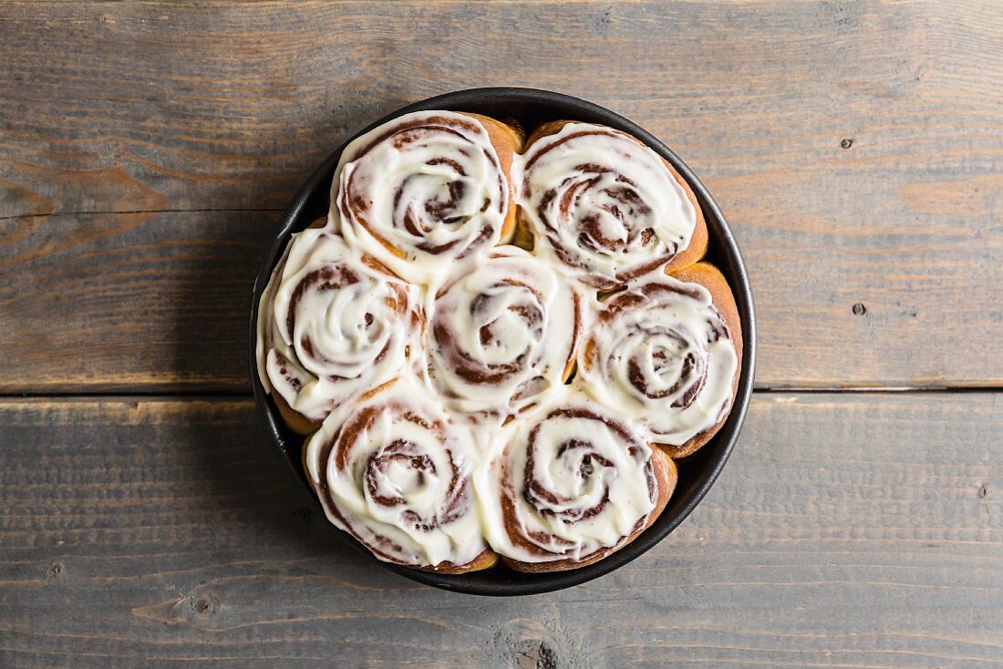 Cinnamon and cardomom buns in a pan with vanilla cream cheese frosting