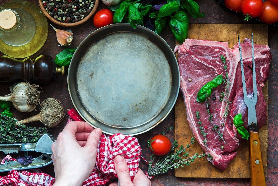 Rohes T-Bone-Steak mit Pfanne und verschiedenen Zutaten