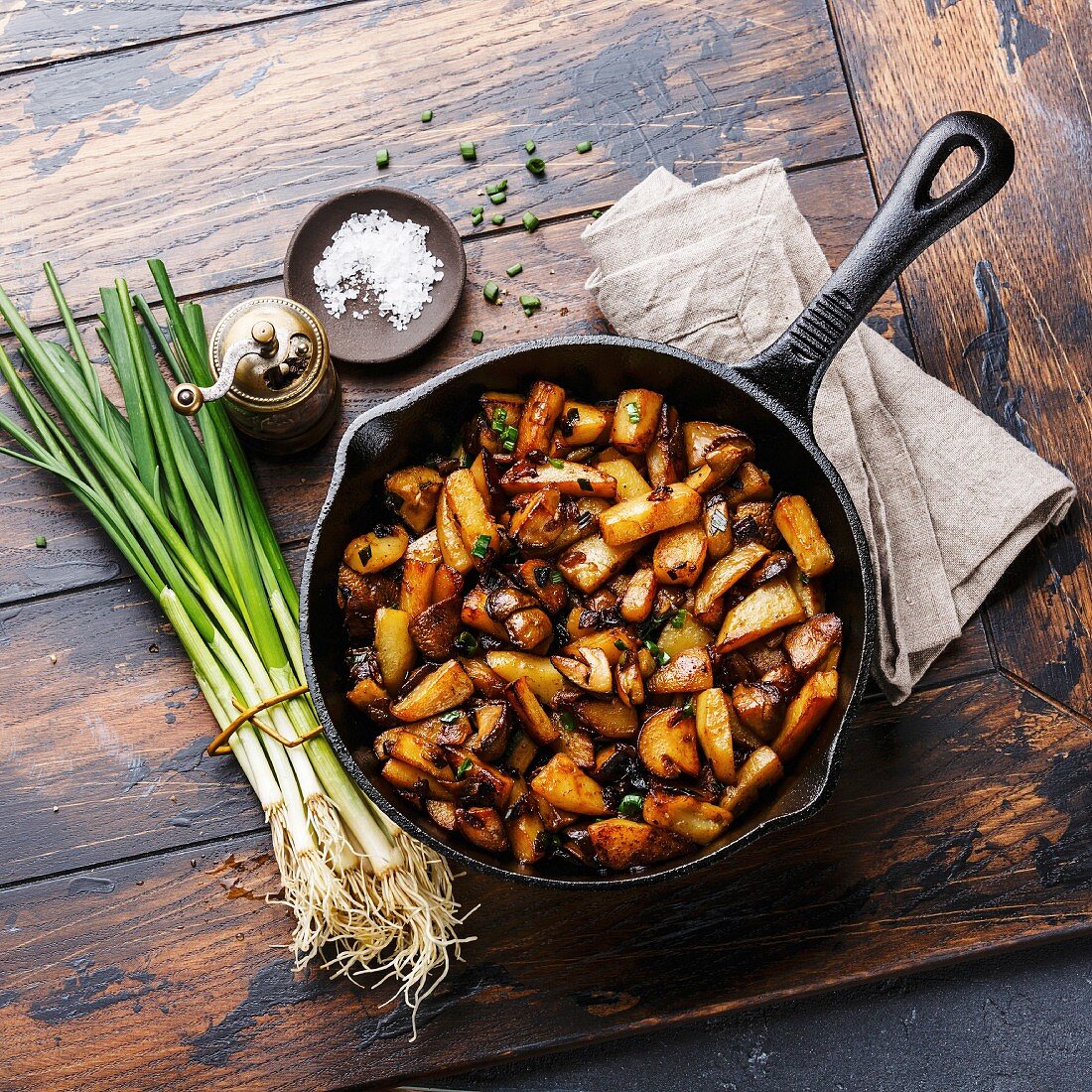 Fried potatoes roasted with porcini mushrooms in cooking pan on wooden background
