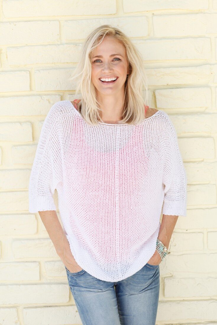 A blonde woman wearing a red top under a white jumper and jeans