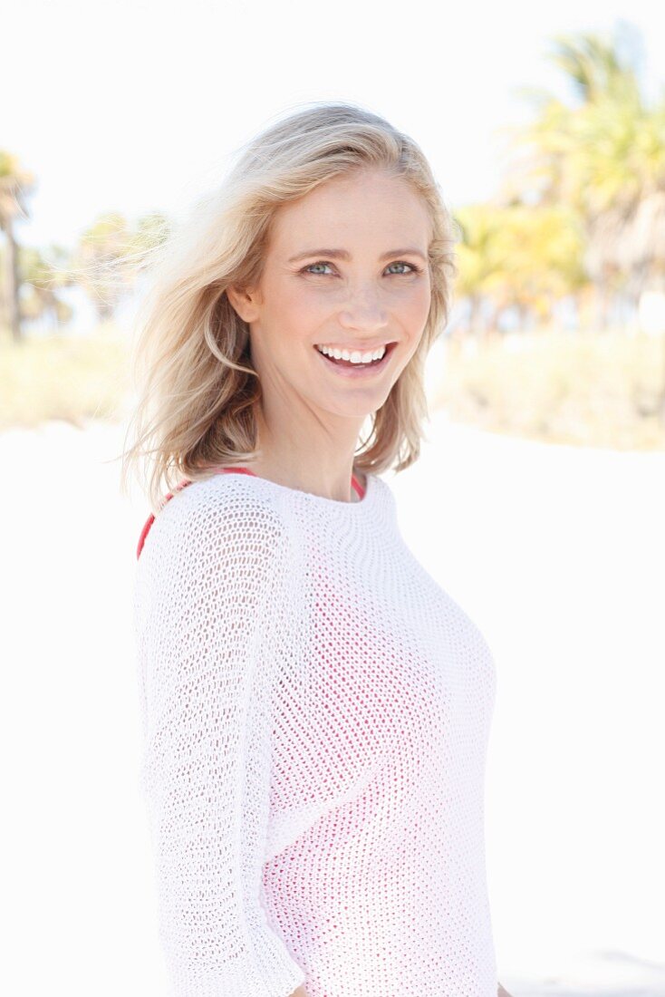 A blonde woman wearing a red top under a white jumper