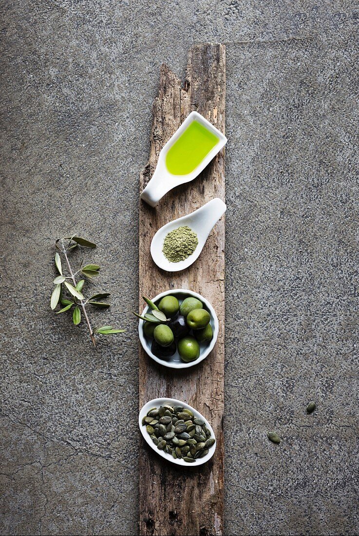 Green food: olive oil, macha tea, olives, pumpkin seed on grey background