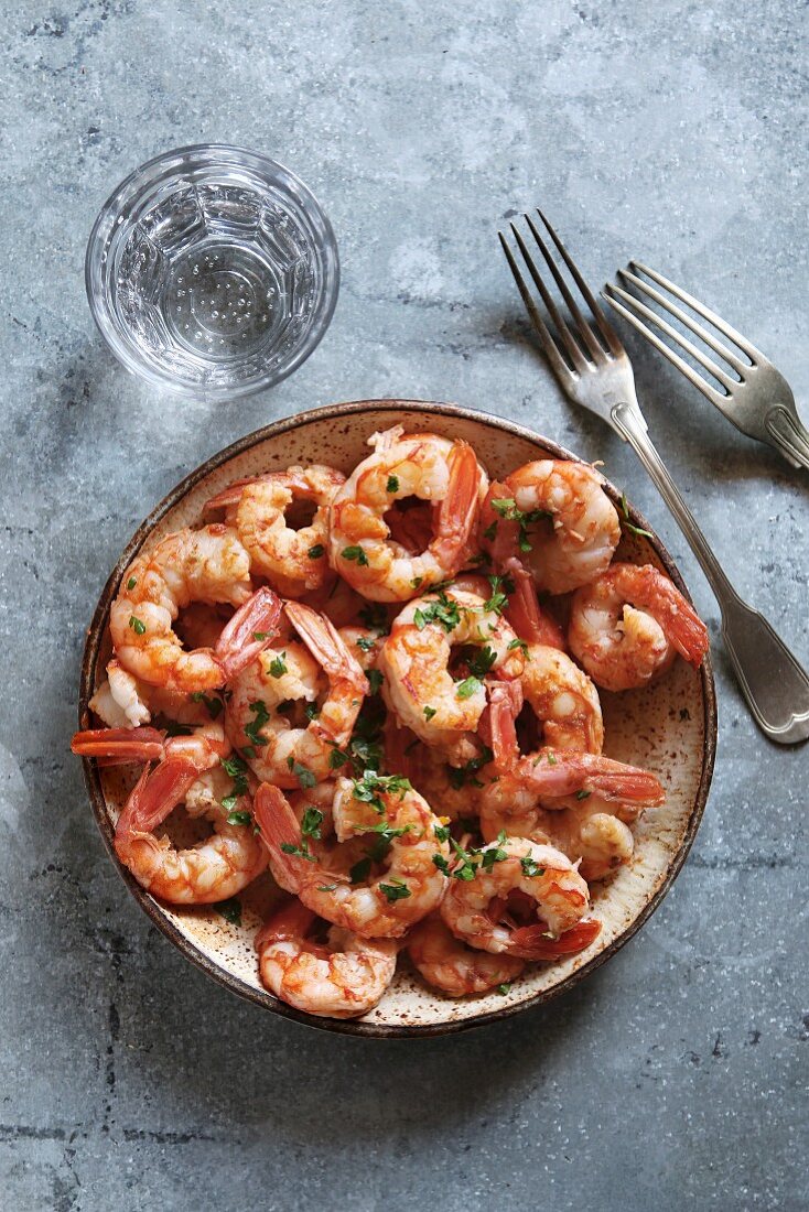 Sauteed shrimp with garlic, parsley and anchovy butter on a plat with a glass of sparkling water