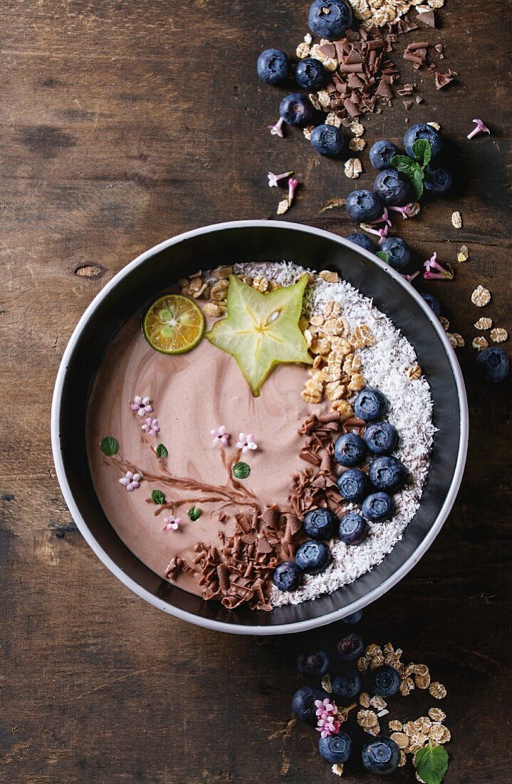 Smoothie bowl:Chocolate yogurt with blueberries, granola, coconut, lime and carambola over dark wooden texture background