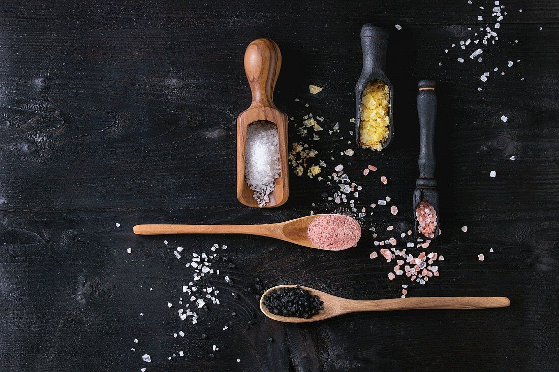 Variety of different colorful salt yellow saffron, pink, black himalayan, white sea and fleur de sel in wooden spoons