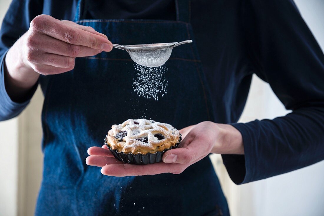 Frauen bestäubt vegane Blaubeertarte mit Puderzucker