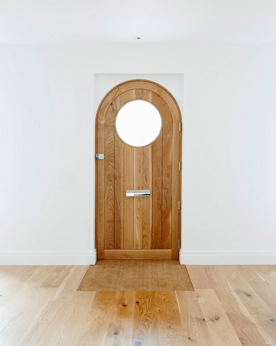 Blick auf Eingangstür mit rundem Fensterausschnitt in leerem Raum mit Eichenparkett