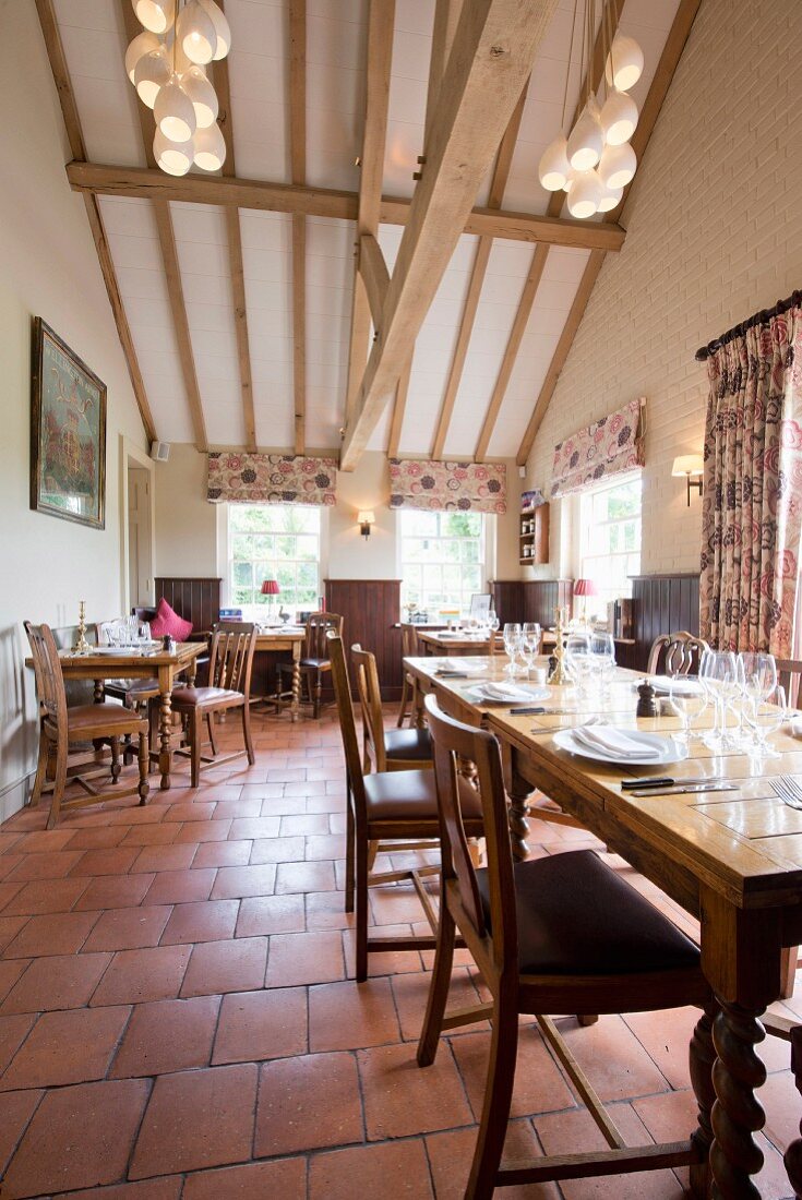 Oak furniture on terracotta floor tiles in restaurant with pale wood-beamed ceiling