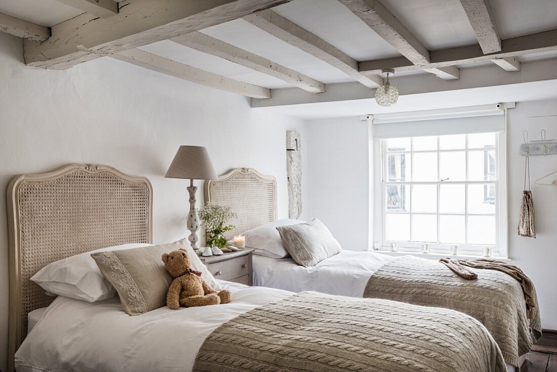 Twin beds with rattan headboards in bright, vintage bedroom with wood-beamed ceiling