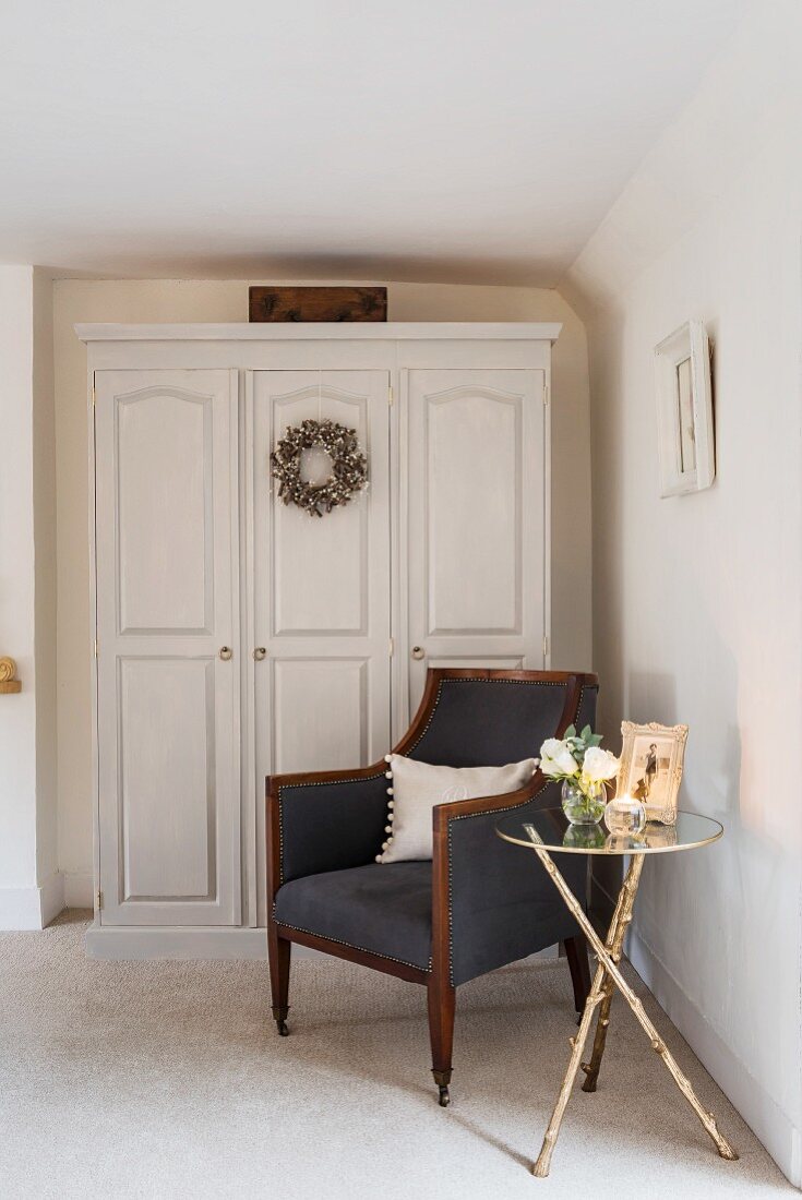 Side table and armchair in front of wardrobe with panelled doors