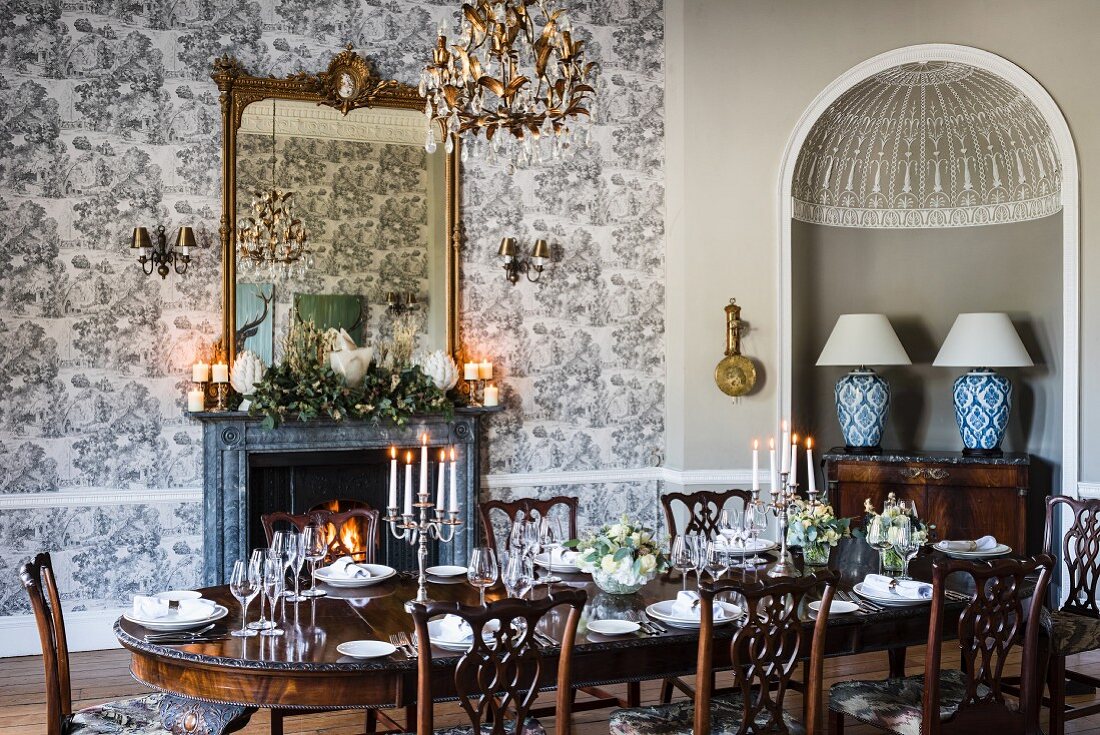 Elegantes Esszimmer mit festlich gedecktem Tisch, Kamin, Goldrahmenspiegel und Toile de Jouy Tapete