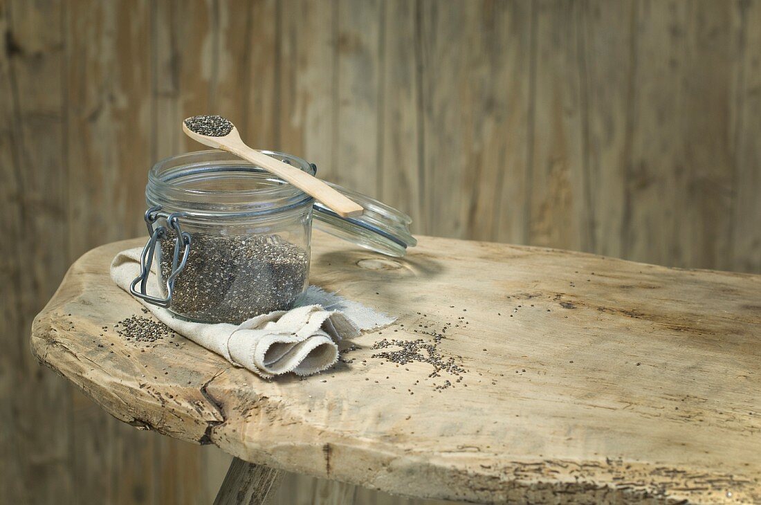 Chiasamen in Einem Vorratsglas und auf einen Holzlöffel auf rustikalem Holzhocker