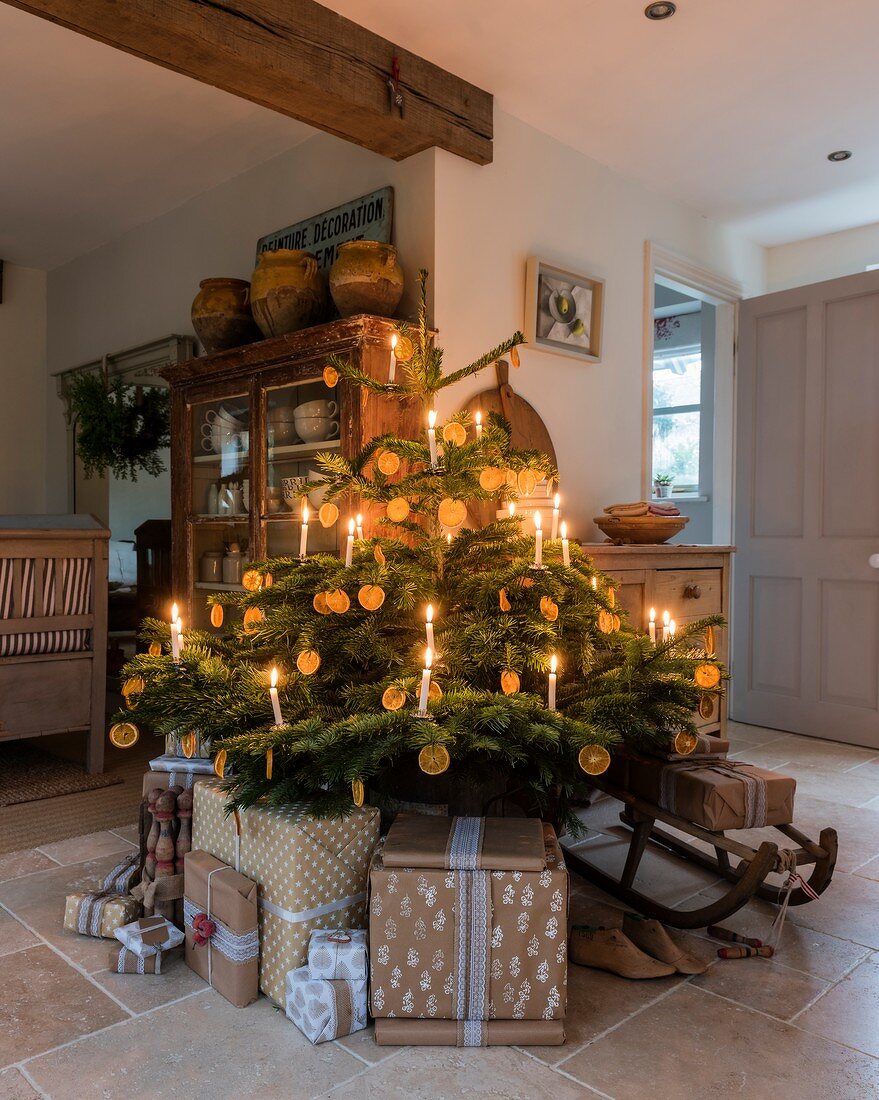 Presents around base of Christmas tree decorated with candles and slices of orange