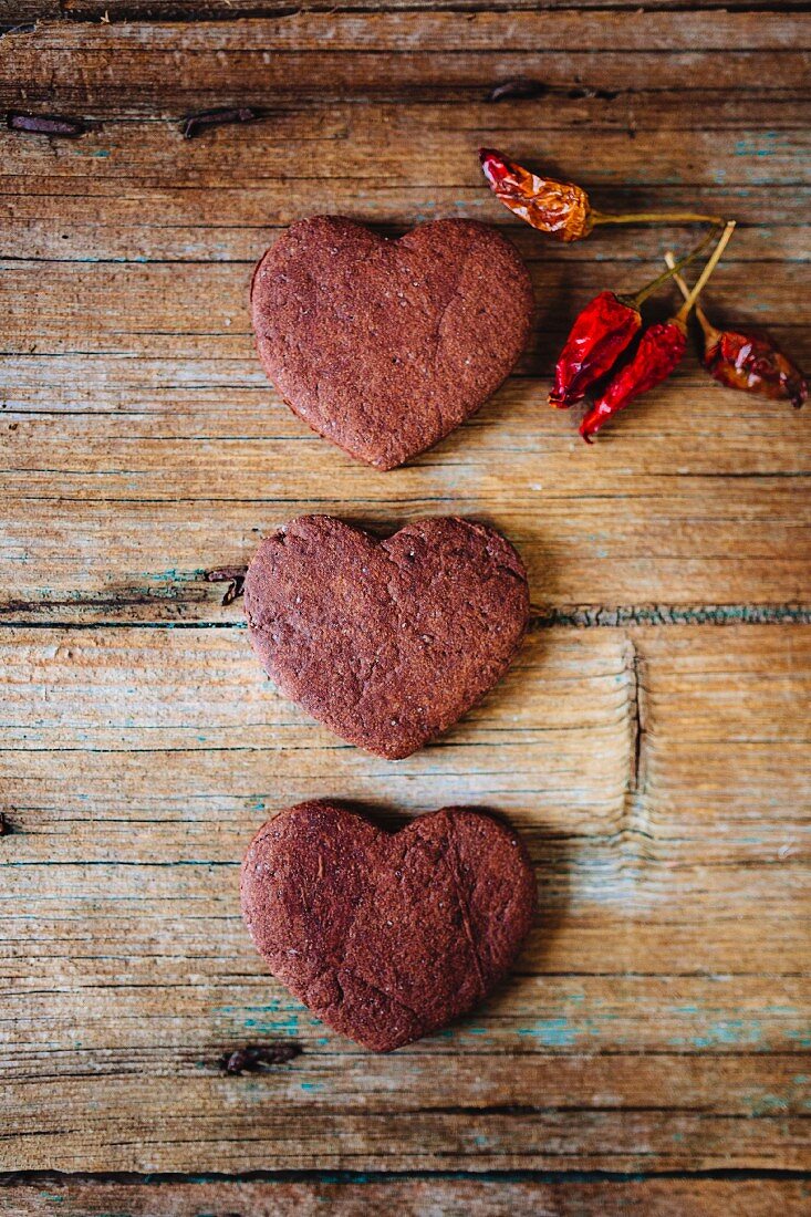 Three heart-shaped chocolate shortbreads and dried chili pods on wood