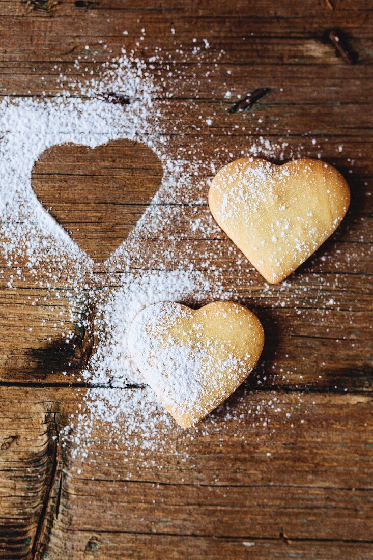 Two heart-shaped shortbreads sprinkled with icing sugar on wood