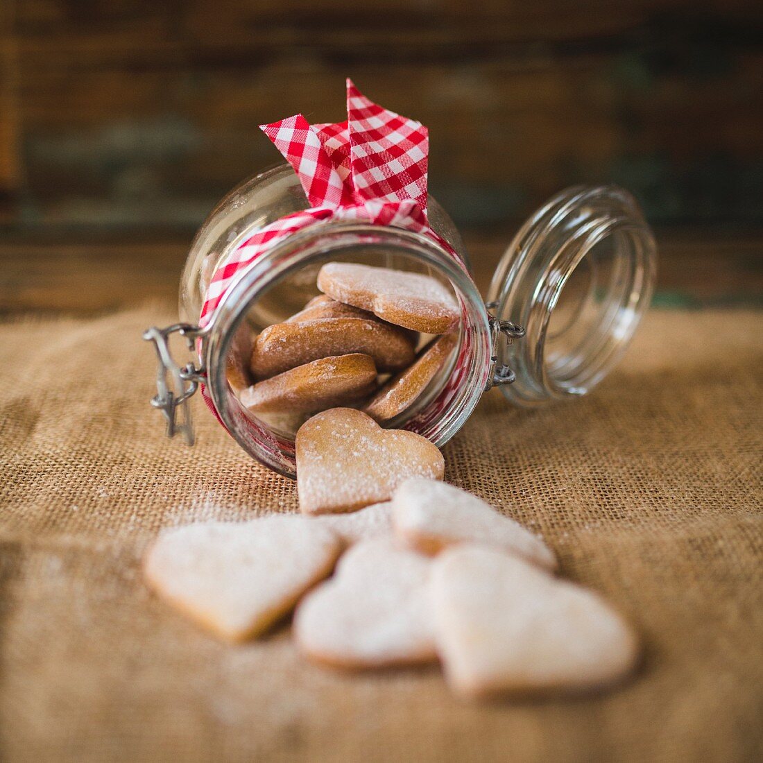 Preserving jar of heart-shaped shortbreads sprinkled with icing sugar on jute
