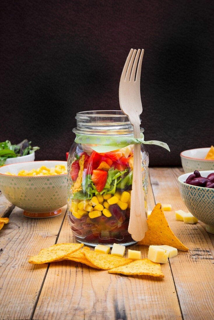 Glass of Tex-Mex salad and ingredients on wood