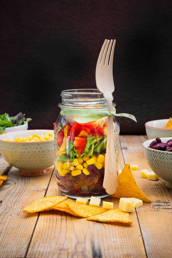 Tex-Mex-Salat im Glas und Zutaten auf Holztisch