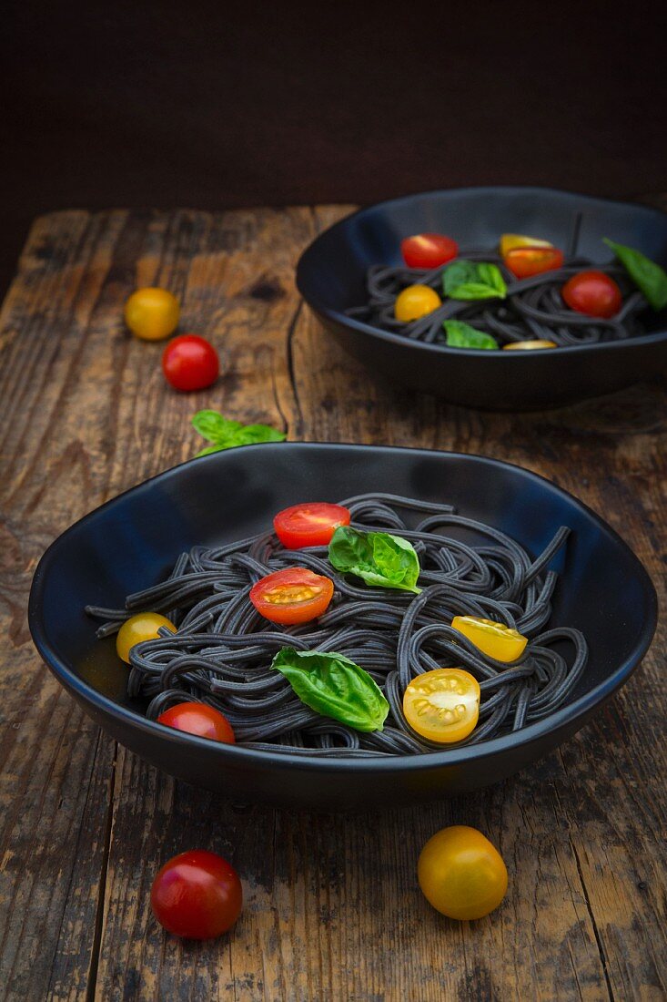 Two bowls of Spaghetti al Nero di Seppia with tomatoes and basil leaves