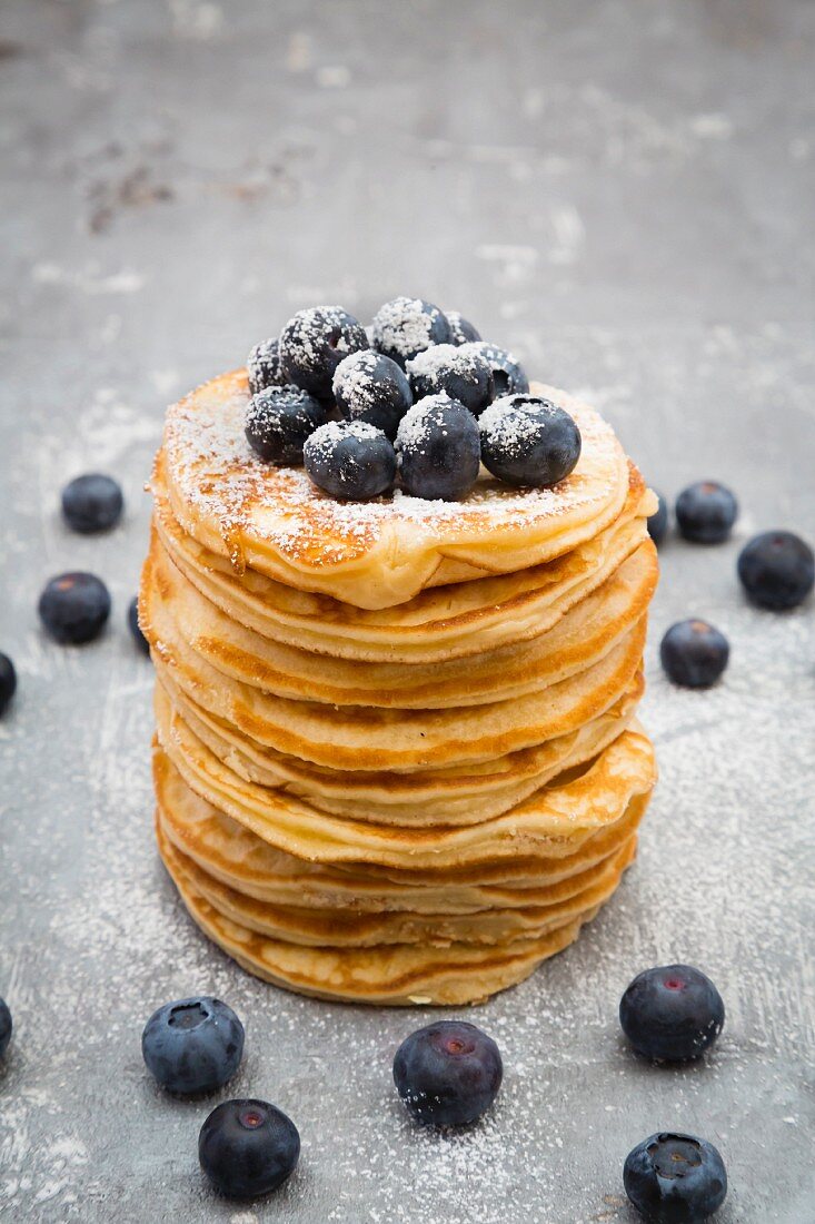 A stack of pancakes with blueberries and icing sugar