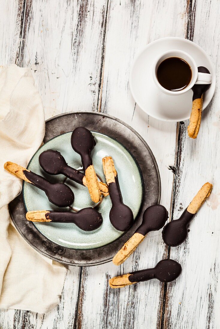 Löffelförmige Kekse mit Schokoladenglasur auf Teller und einer Tasse Espresso