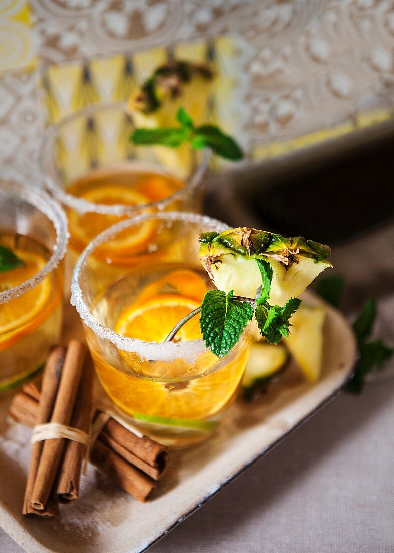Cocktail mit Weißwein, Zimt, Ananas und Orangenscheiben im Glas mit Zuckerrand