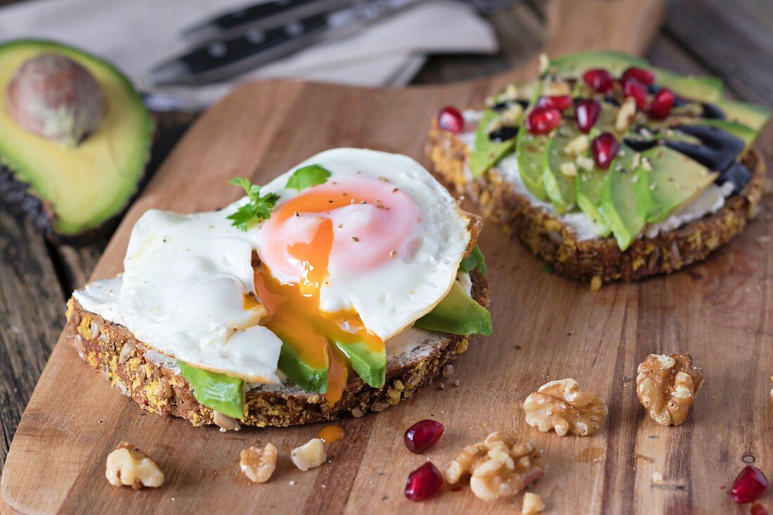 Protein bread slice with cream cheese, sliced avocado and fried egg on wooden board