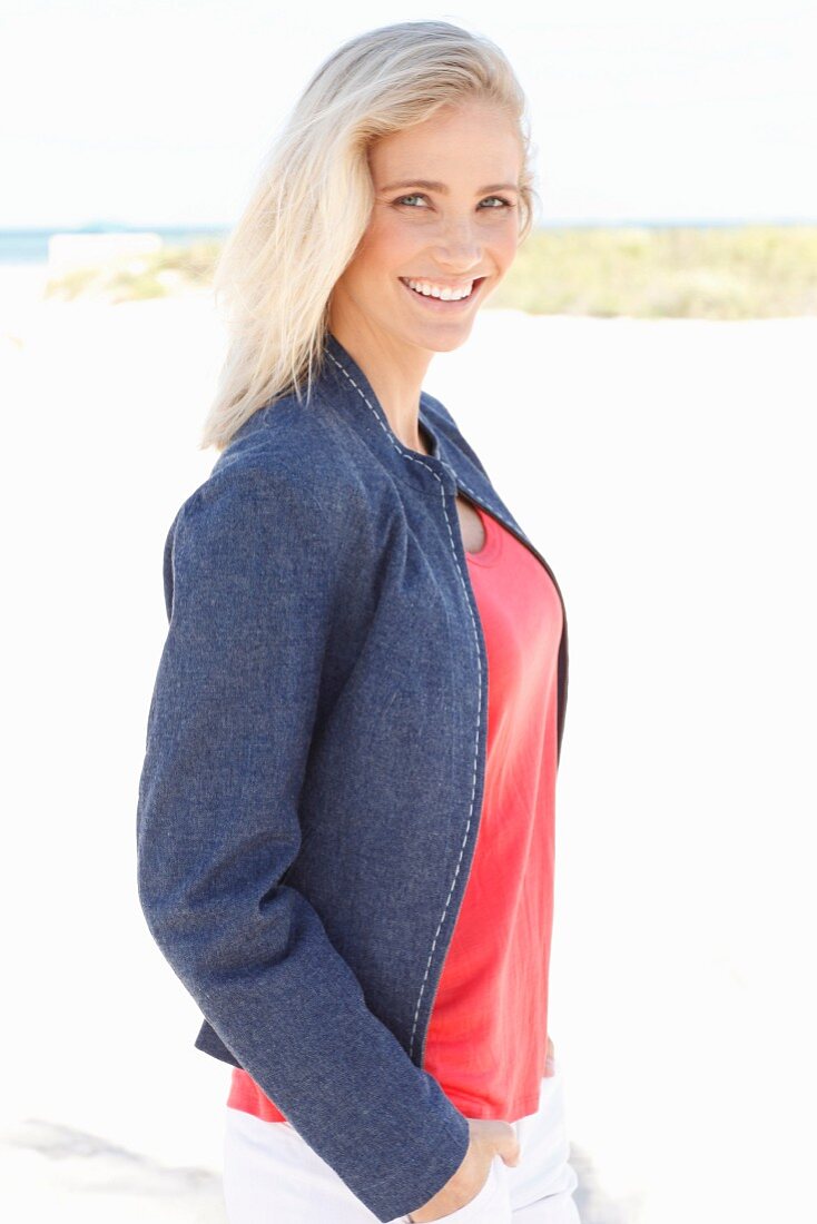 A blonde woman wearing a red top, a denim jacket and white trousers