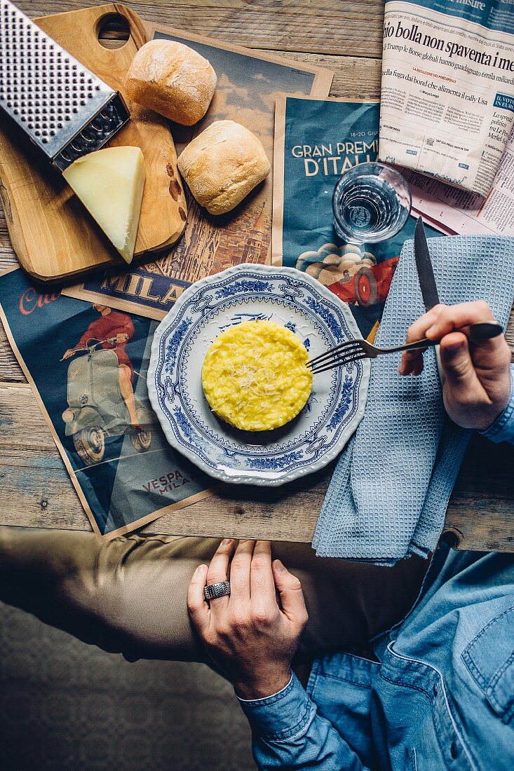 Risotto Milanese on a rustic wooden table with a newspaper, cheese and bread rolls