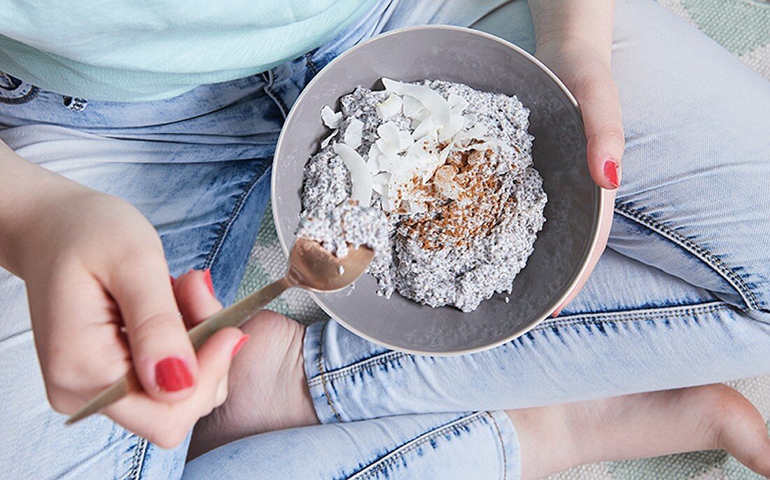 A woman eating vegan chia pudding with coconut milk and cinnamon