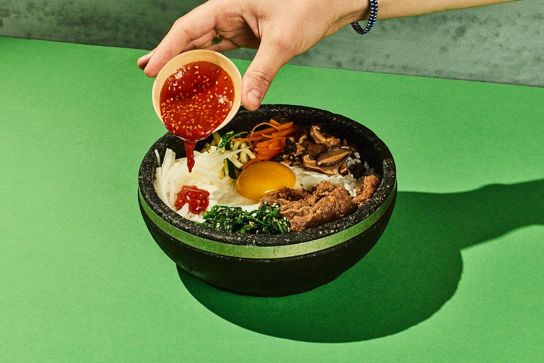 Bibimbap (a colourful rice bowl with beef, vegetables and a fried egg, Korea) with gochujang sauce