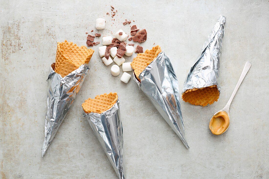 Eiswaffeln, Mini-Marshmalllows, Erdnusscreme und Schokoraspeln für Campfire-Cones