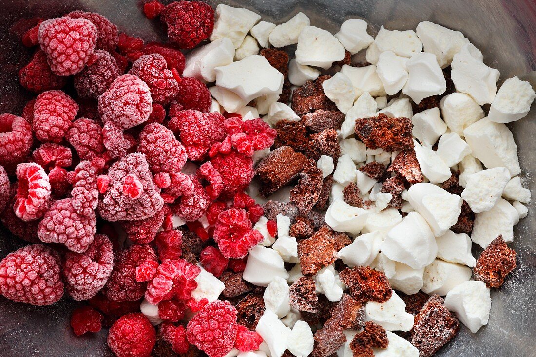 Frozen raspberries, crumbled meringue and chocolate biscuits for an ice bombe cake