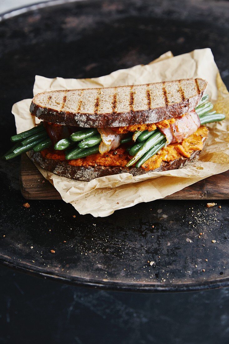 A farmhouse bread sandwich with bacon-wrapped green beans and red lentils