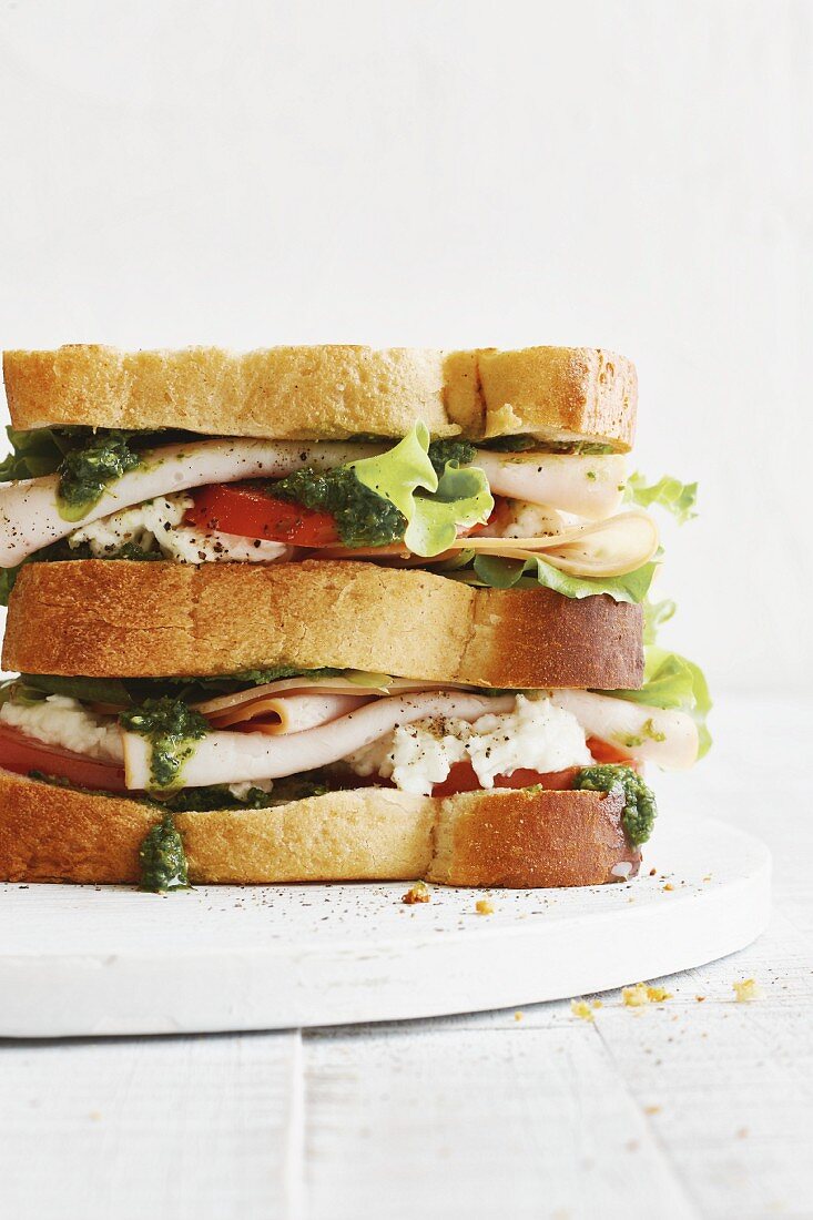 A club sandwich with turkey breast, tomatoes, mozzarella and salsa verde