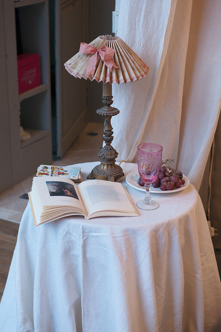 Open book and lamp on small table with white tablecloth