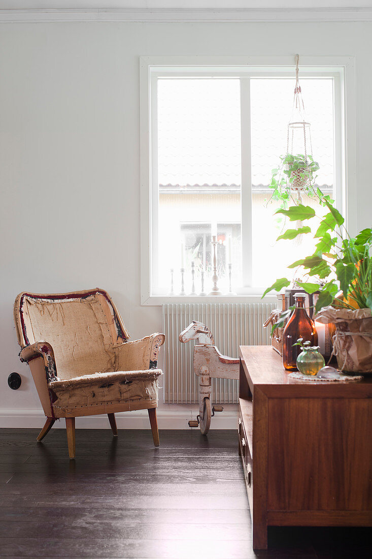 Vintage Sessel und Dreirad-Pferd vor Fenster, im Vordergrund Sideboard mit Zimmerpflanze