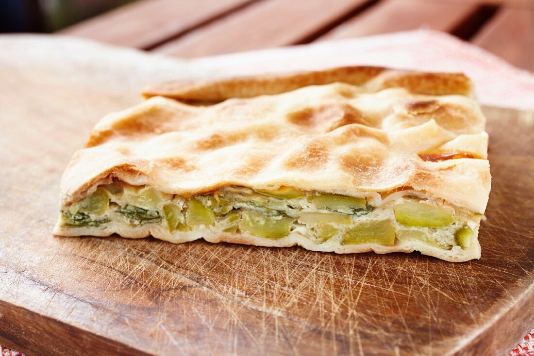 A slice of courgette, egg and quark pie with flaky pastry on a wooden chopping board