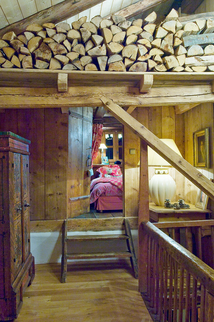 Landing with firewood stacked on beams in rustic chalet; view into bedroom