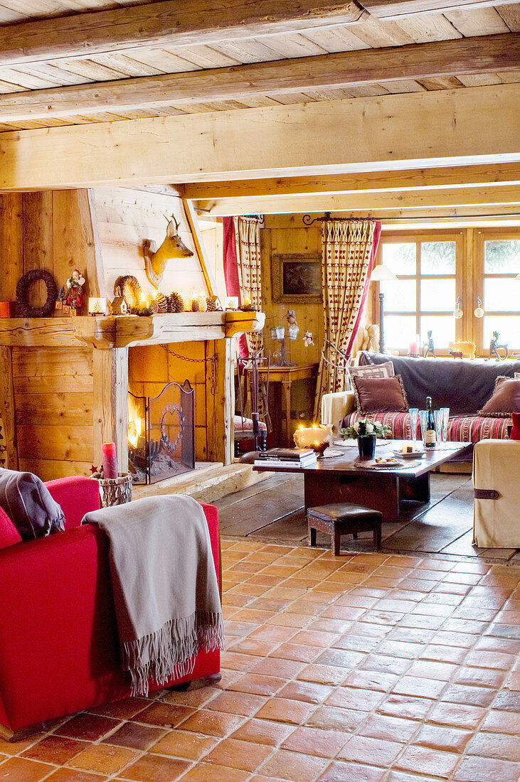 Red armchair, fireplace clad in wood, sofa set and coffee table in open-plan chalet interior